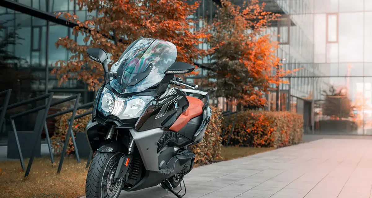 Skuter BMW C650 GT z brązowym siedzeniem na tle nowoczesnego budynku i jesiennych drzew. Dane techniczne tego modelu są imponujące.