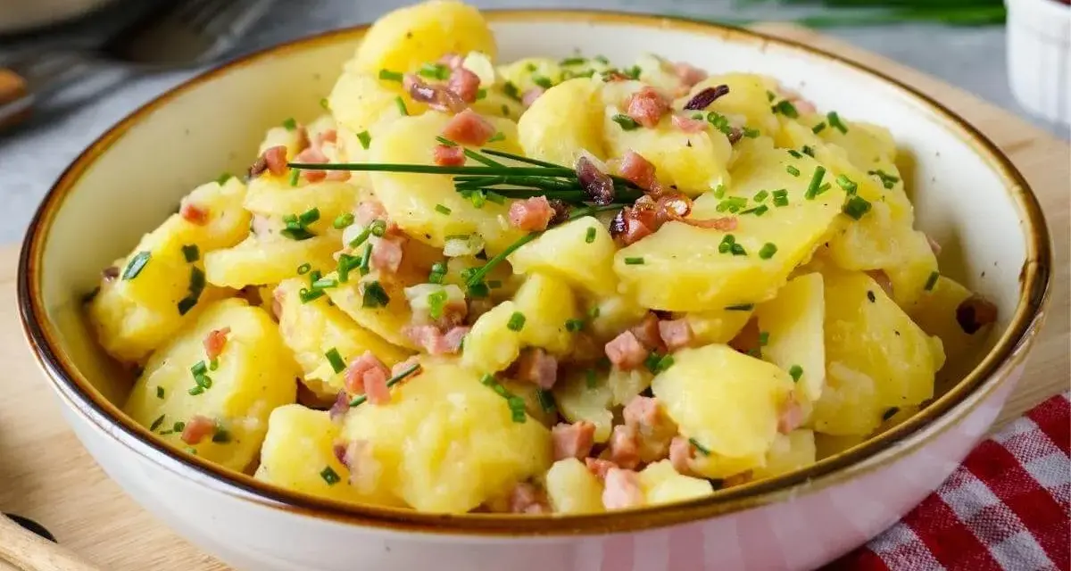 Schüssel mit warmem Kartoffelsalat, garniert mit Speckwürfeln und Schnittlauch. Ein Klassiker, der immer schmeckt!
