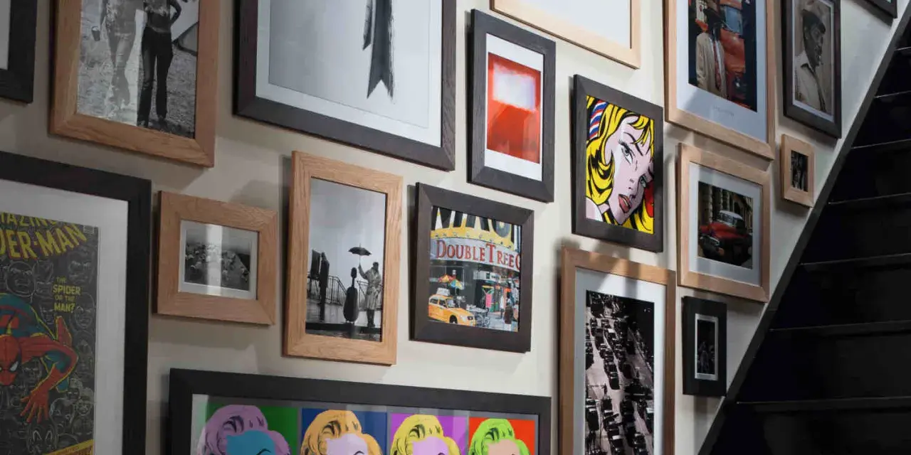 Un mur couvert de tableaux, dont des portraits de Marilyn Monroe, une scène de rue et une affiche de Spider-Man, le tout dans un cadre.