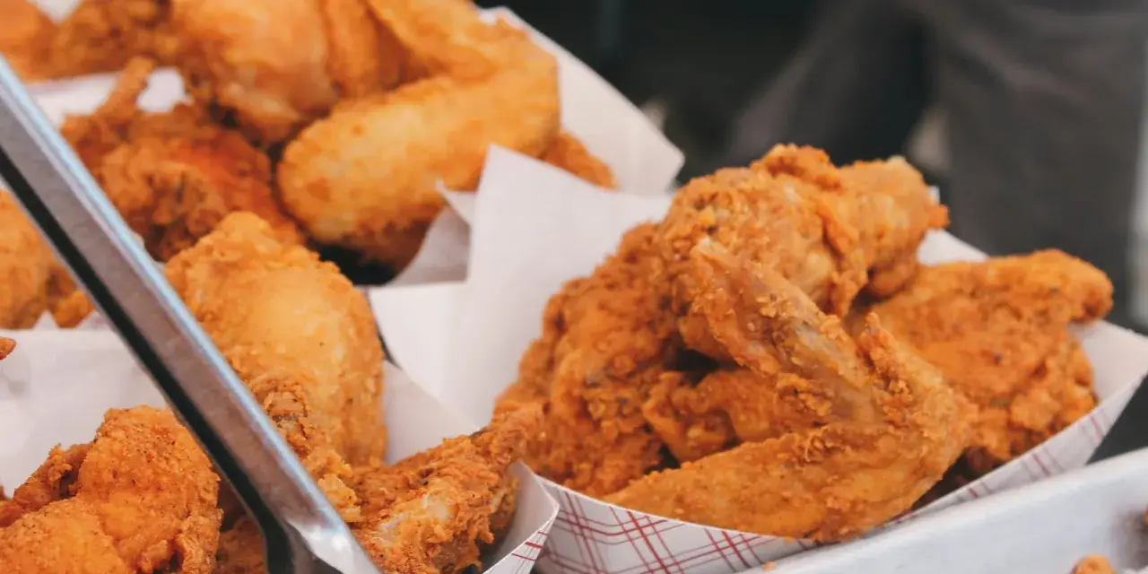 Un surtido de crujiente pollo frito en recipientes de cartón. Las piezas doradas y sabrosas invitan a disfrutar de este clásico.