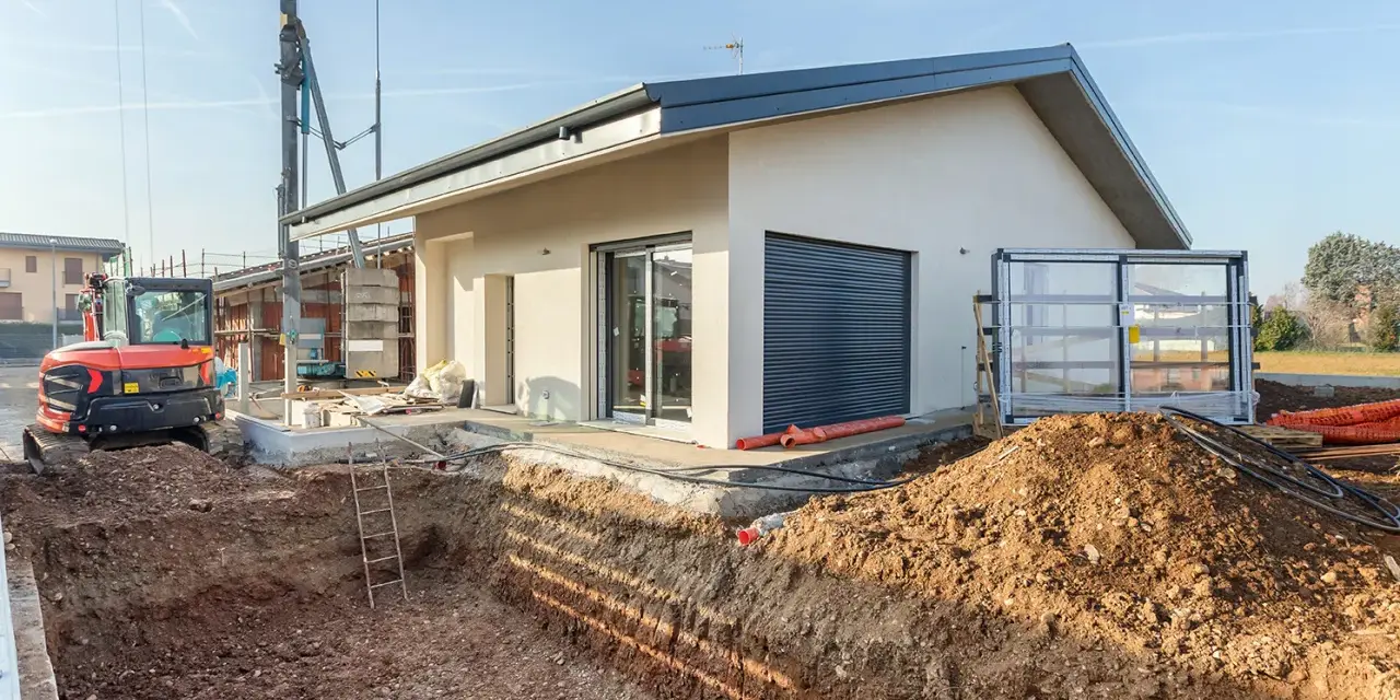 Budowa domu 70m2. Wykop pod fundamenty, koparka i częściowo wykończony budynek.