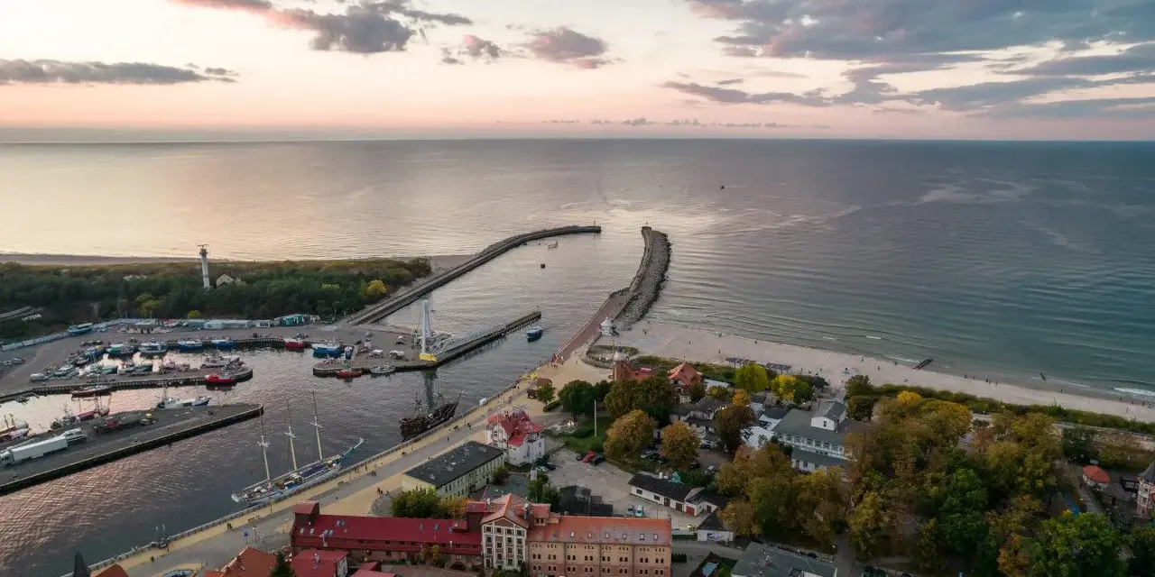Widok z lotu ptaka na port w Ustce z łodziami i latarnią morską w tle.