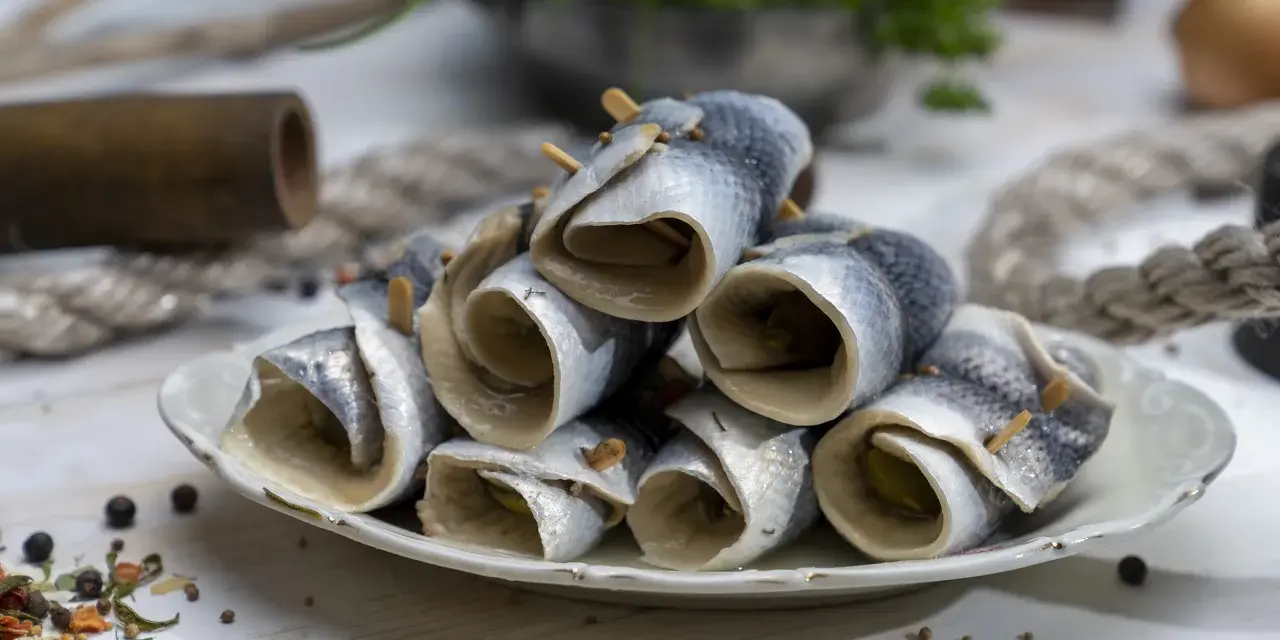 Gestapelte Rollmops Fisch auf einem Teller, garniert mit Gewürzen und Holzspießen.