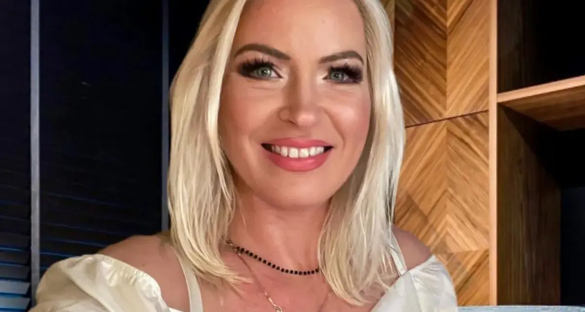 Uśmiechnięta Joanna Janikowska-Samojłowicz w białej bluzce z odkrytymi ramionami, z naszyjnikami na szyi.