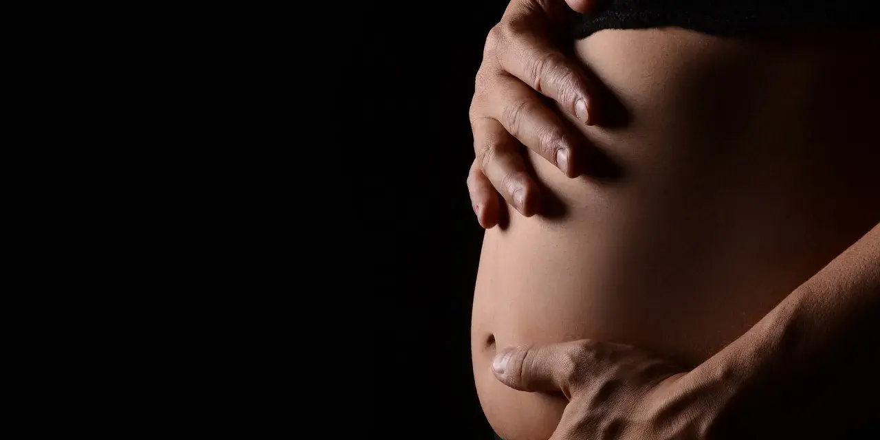 Mani che accarezzano un pancione. La ricerca sulle cause dell'autismo in gravidanza è complessa e in continua evoluzione.