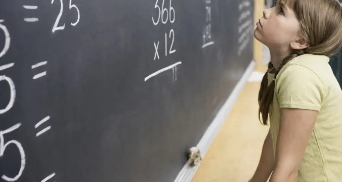 Dziewczynka zmagająca się z zadaniem z matematyki na tablicy. Czy dysleksja a matematyka to trudne połączenie?