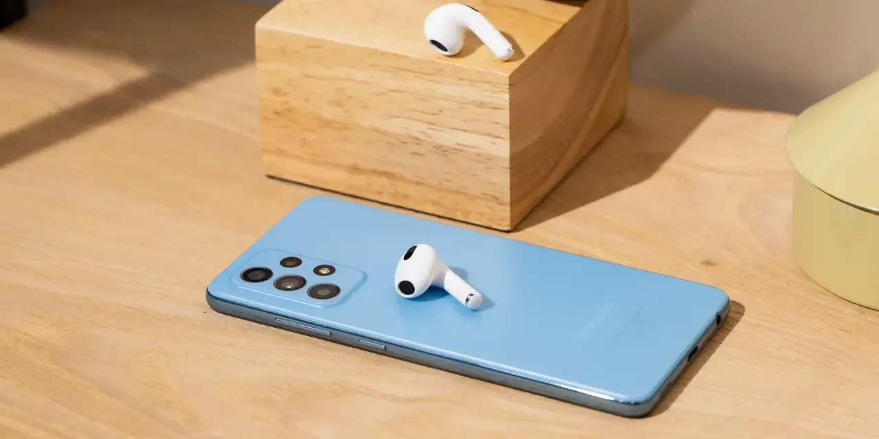 AirPods liegen auf einem blauen Samsung-Smartphone und einem Holzblock.