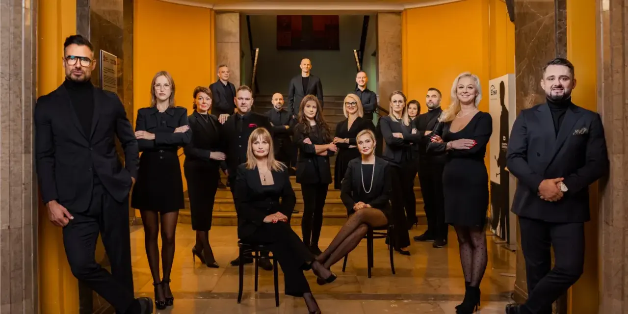 Grupa profesjonalistów w czarnych strojach pozuje w eleganckim wnętrzu.