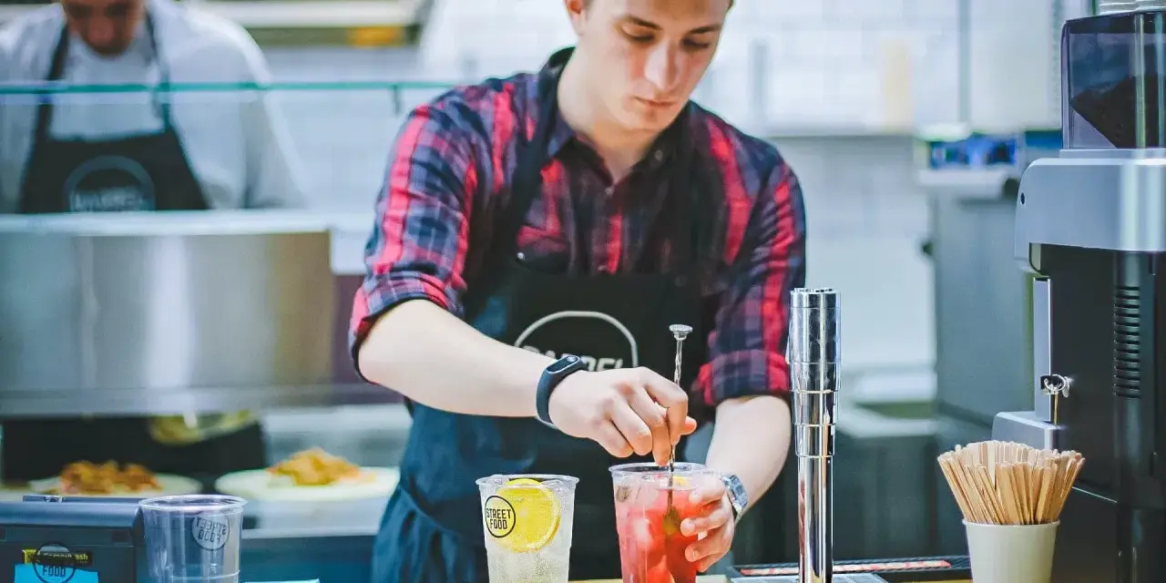 Ein junger Mann, der als Werkstudent 20 Stunden pro Woche arbeitet, mixt Getränke in einem Streetfood-Laden.