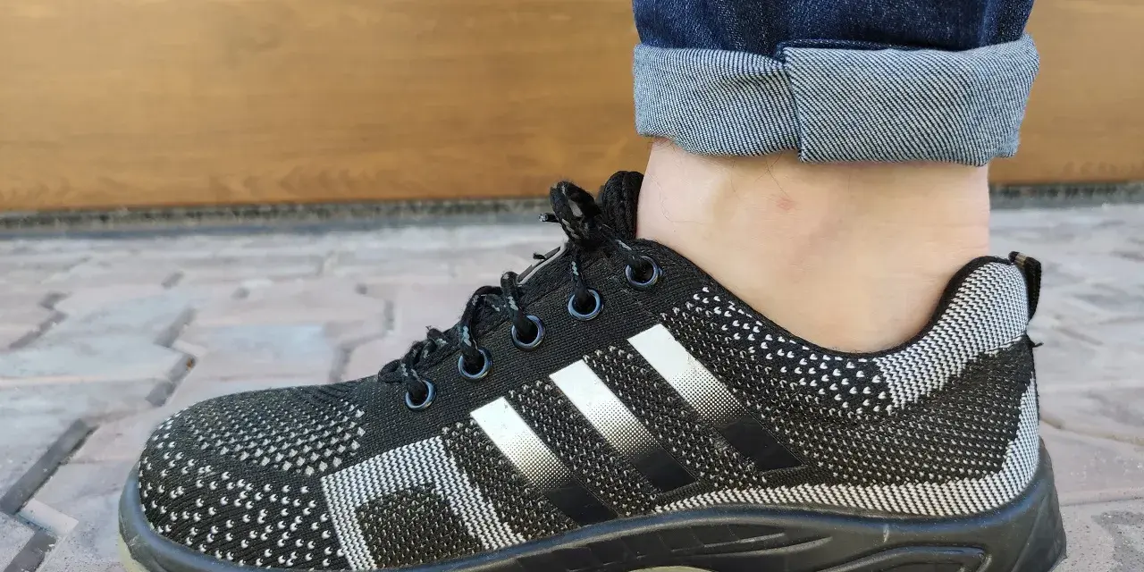 Czarne buty sportowe z białymi paskami i podwiniętymi nogawkami jeansów. Idealny przykład, jak podwinąć spodnie.