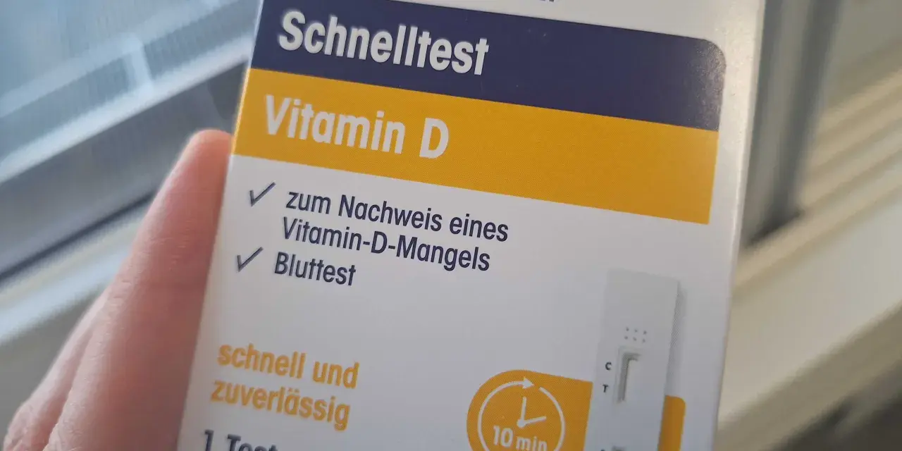 Hand hält eine Verpackung für einen Vitamin-D-Schnelltest mit einem Bluttest-Streifen.