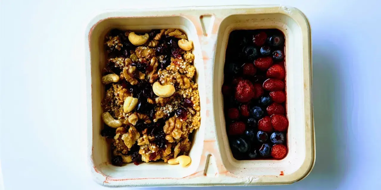 Dwie przegródki pojemnika: jedna z granolą i orzechami, druga z jagodami i truskawkami. Czy kasza jaglana ma gluten? Ta granola wygląda na bezglutenową!