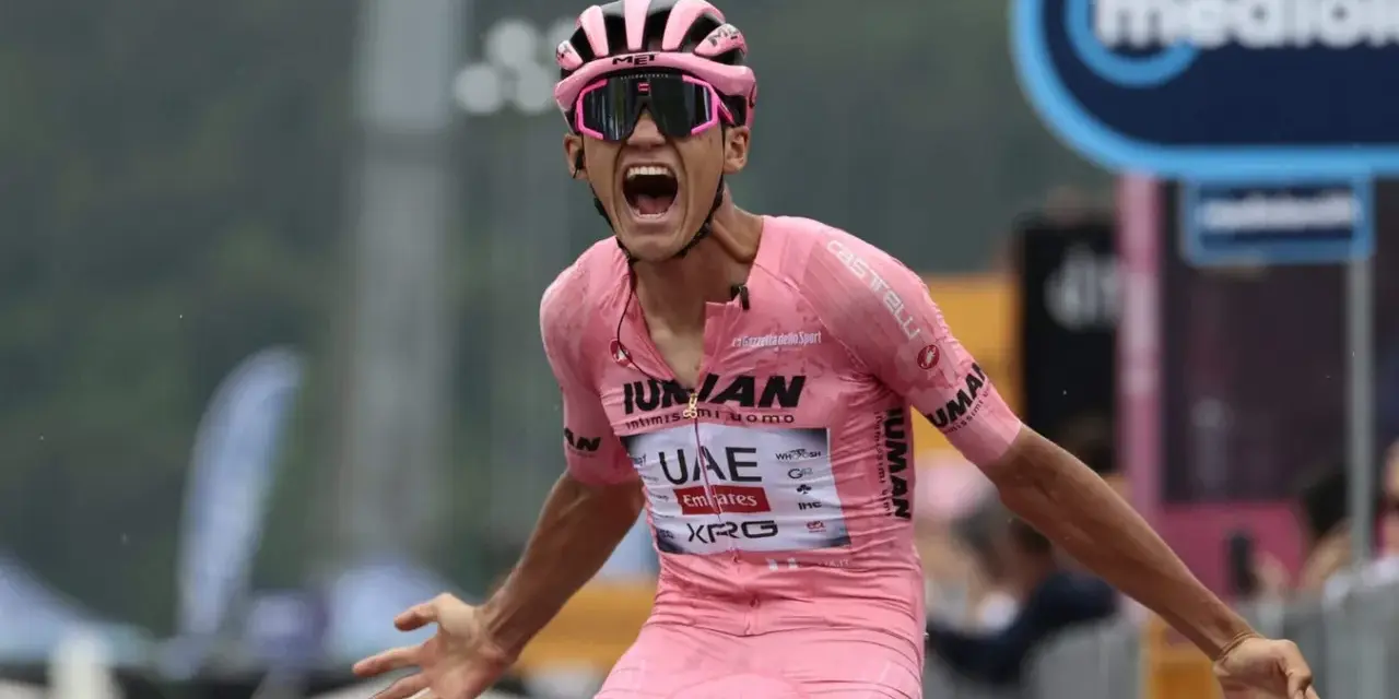 Isaac Del Toro, a cyclist in a pink jersey, screams in triumph, arms outstretched.