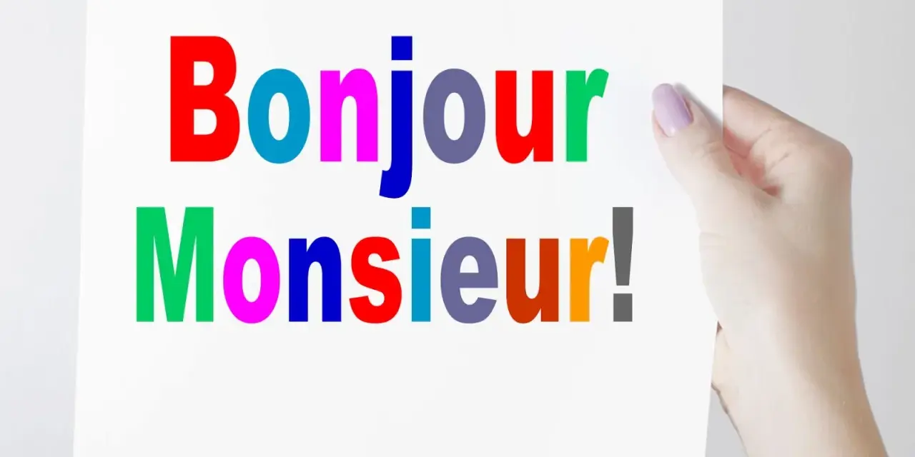 Una mano sostiene un cartel con "Bonjour Monsieur!" escrito en letras de colores.