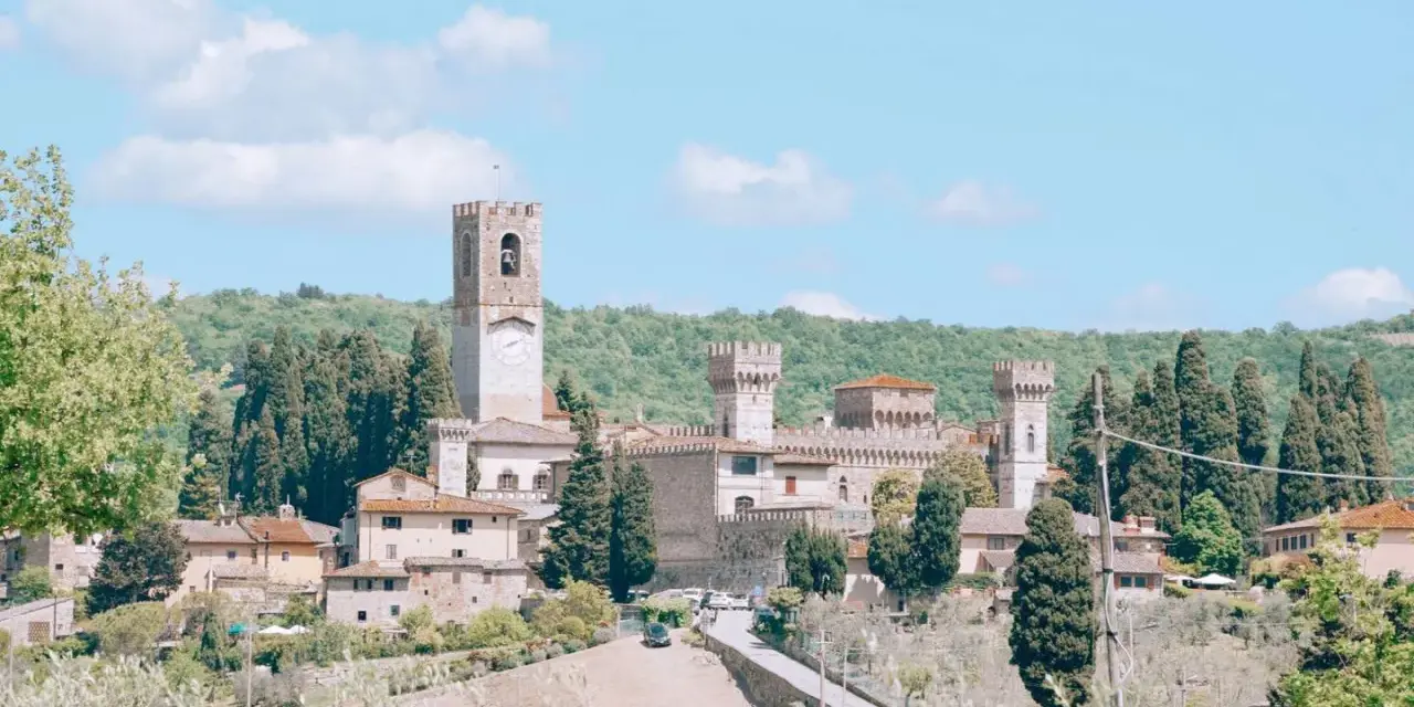 La Badia a Passignano, un borgo medievale toscano con un'imponente torre dell'orologio, circondato da colline verdi e cipressi.