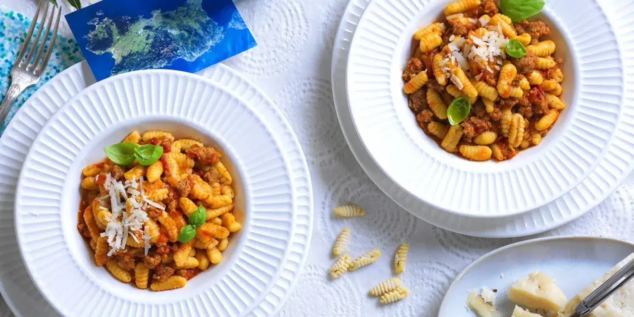 Due piatti di gnocchetti alla campidanese, un assaggio di Sardegna con sugo di salsiccia e pomodoro, guarniti con basilico e parmigiano.