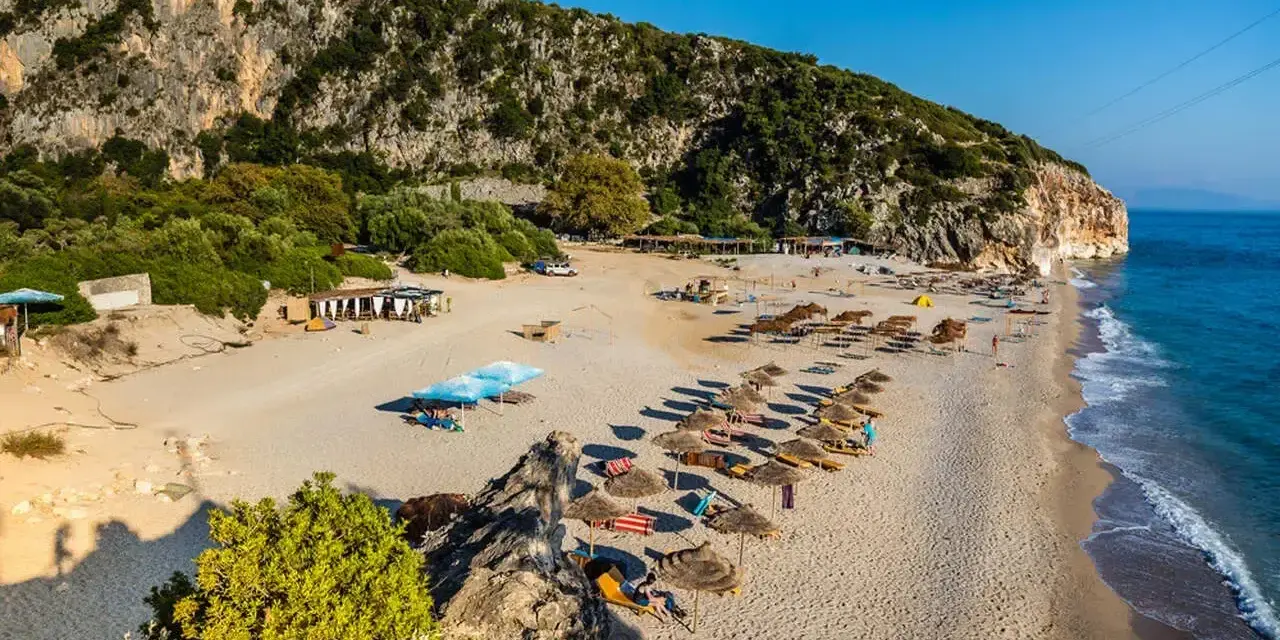 Piękne albania plaże z rzędami parasoli i leżaków, skaliste zbocze i turkusowe morze.