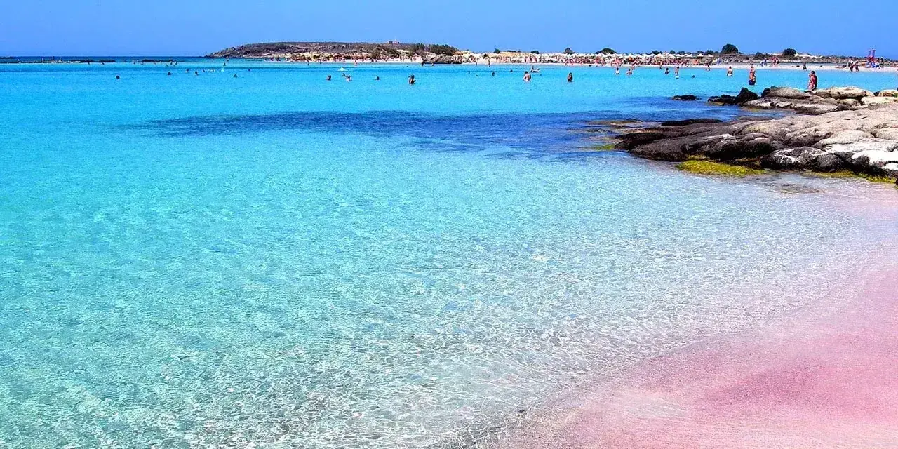Różowy piasek i turkusowa woda na plaży Elafonisi. Ludzie kąpią się w krystalicznie czystym morzu.