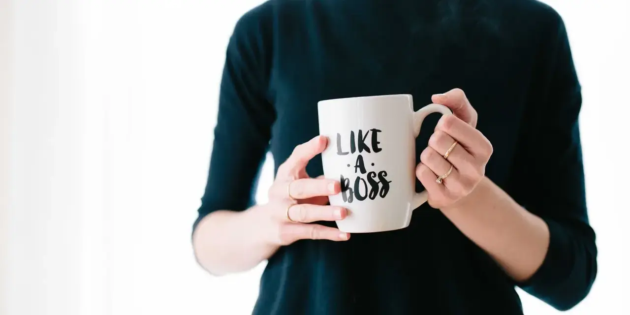 Kobieta trzyma kubek z napisem "Like a boss". Czy to pewność siebie, czy tylko maska na syndrom oszusta?