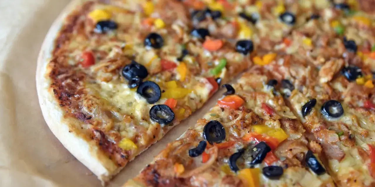 Co to jest pizza? To pyszna, okrągła pizza z oliwkami, papryką i serem, pokrojona na kawałki.