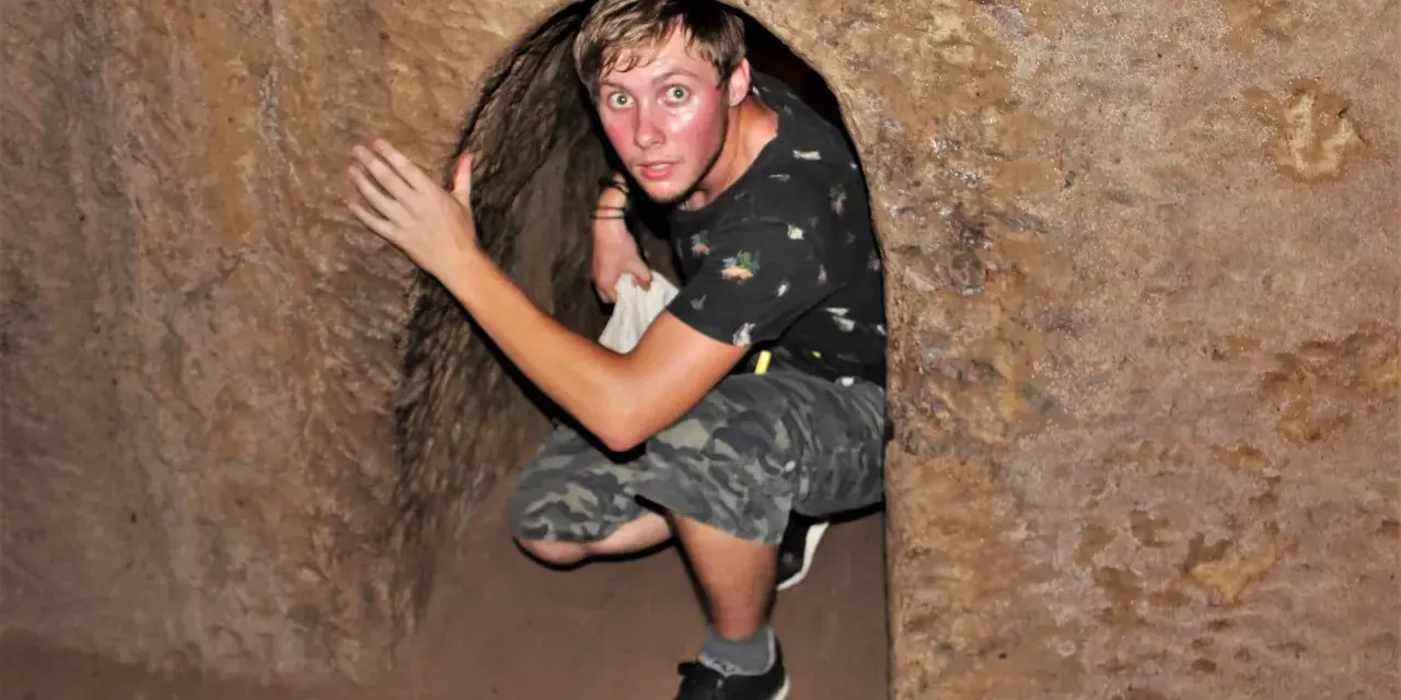 Młody mężczyzna kuca w wąskim tunelu, jednym z historycznych Cu Chi Tunnels.