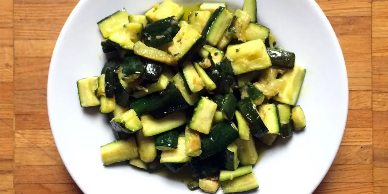 Zucchine in umido, un contorno saporito e leggero, servito in un piatto bianco su un tagliere di legno.