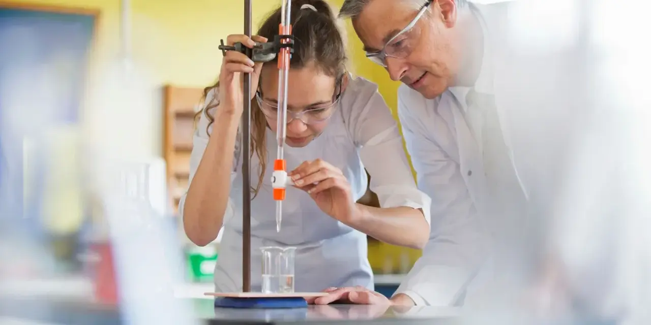 Schülerin bei chemischem Experiment mit Lehrer. Perfekt für die Ausbildung mit Abitur NRW.