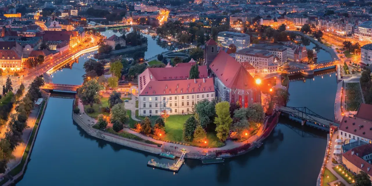 Ostrów Tumski we Wrocławiu nocą, z oświetlonymi budynkami i rzeką. To jedno z najpiękniejszych miejsc Wrocławia.