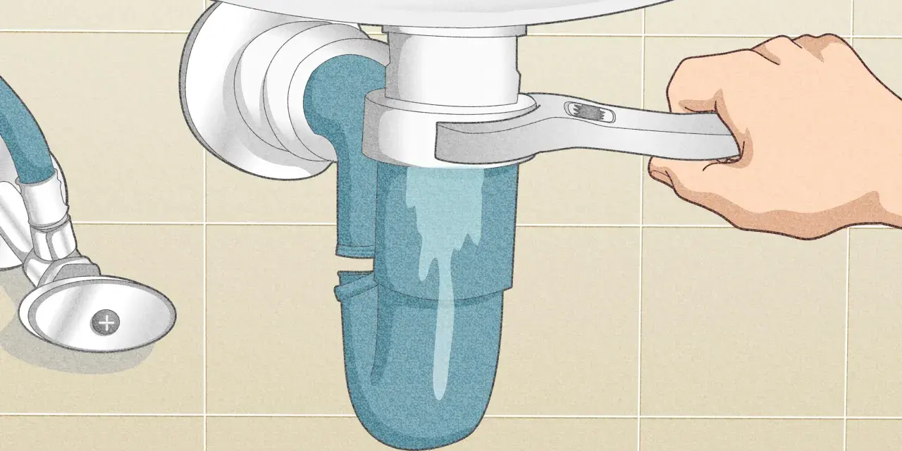 A hand uses a wrench to loosen a sink trap, a step in how to clean a sink drain. Water drains into a bucket below.