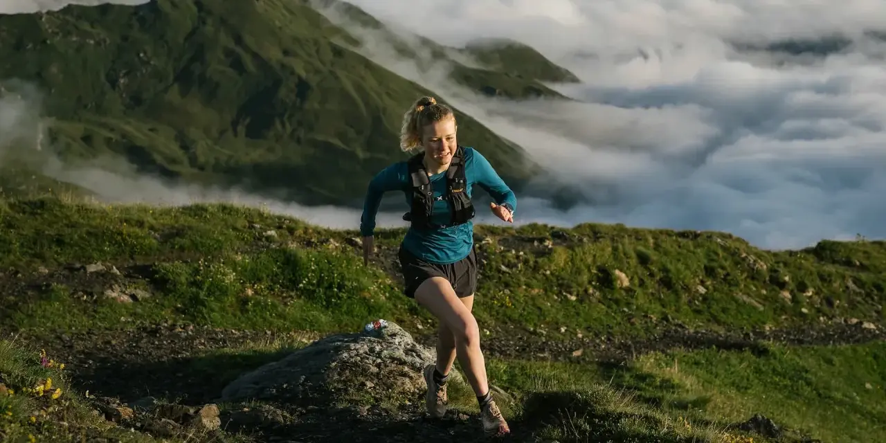 Donna corre su sentiero montano, immersa nella nebbia. Il trail running significato è libertà e sfida.