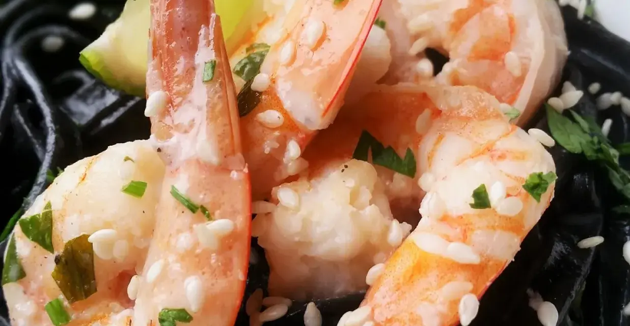 Krewetki z czarnym makaronem, posypane sezamem i natką pietruszki, z kawałkiem limonki.