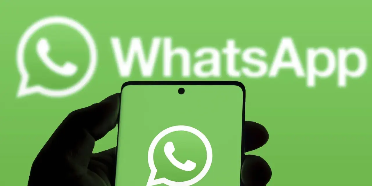 Hand hält Smartphone mit WhatsApp-Logo vor grünem Hintergrund.