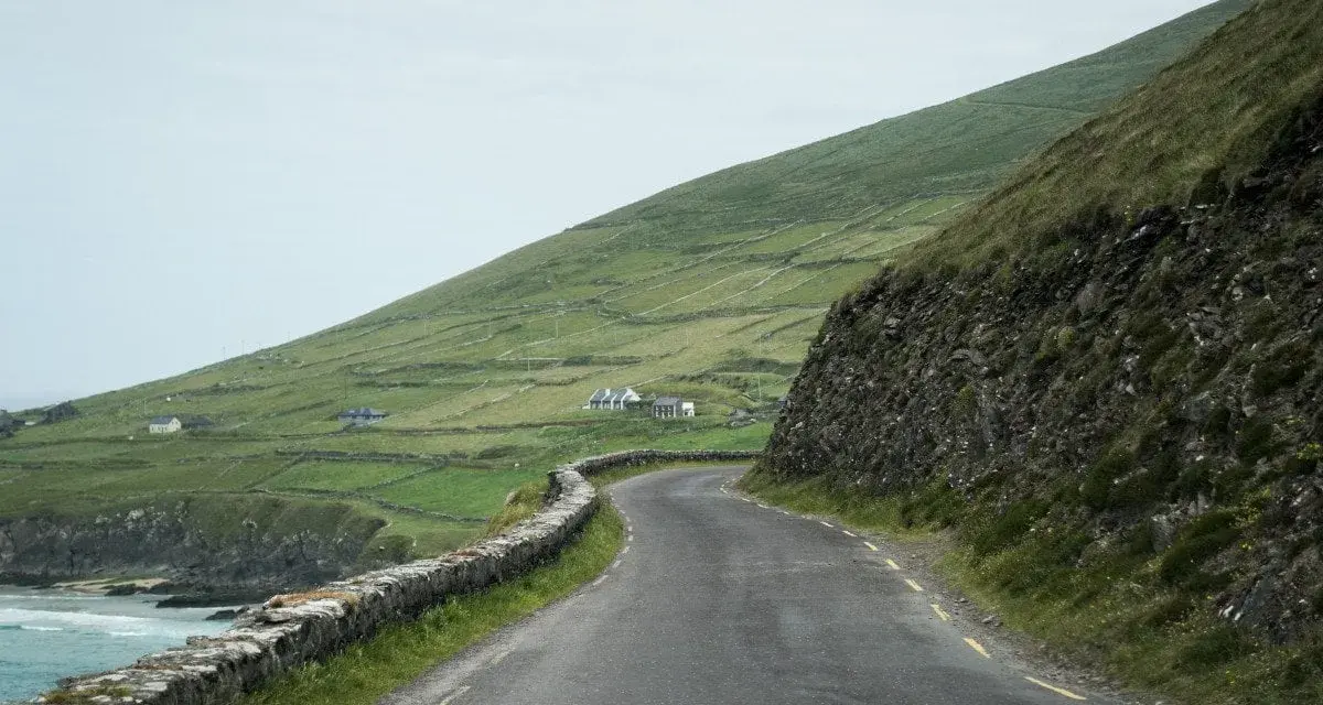 A winding road along the coast of Ireland, perfect for renting a car and exploring the dramatic green hills and stone walls.