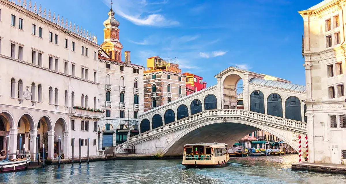 Venezia, il Canal Grande con il Ponte di Rialto e il Fondaco dei Tedeschi sullo sfondo. Una motonave naviga sull'acqua.