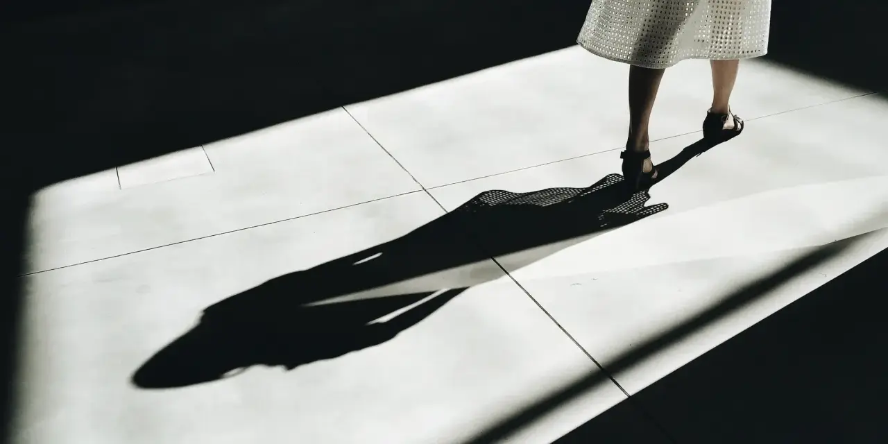 Długa, dramatyczna cień osoby w białej sukience na jasnej posadzce. Jakby zniknęła, zostawiając tylko ślad, niczym w przypadku ghostingu. Co to znaczy?