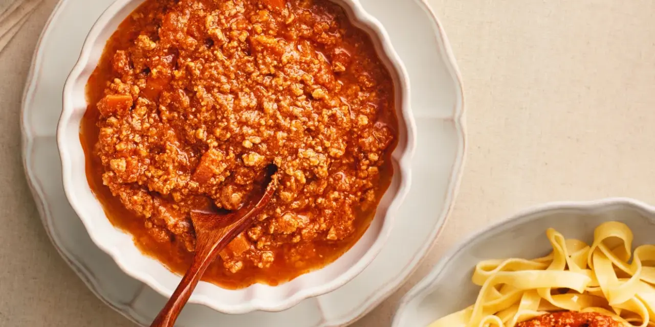 Gęsty, aromatyczny sos do spaghetti bolognese w miseczce, obok porcji makaronu tagliatelle.