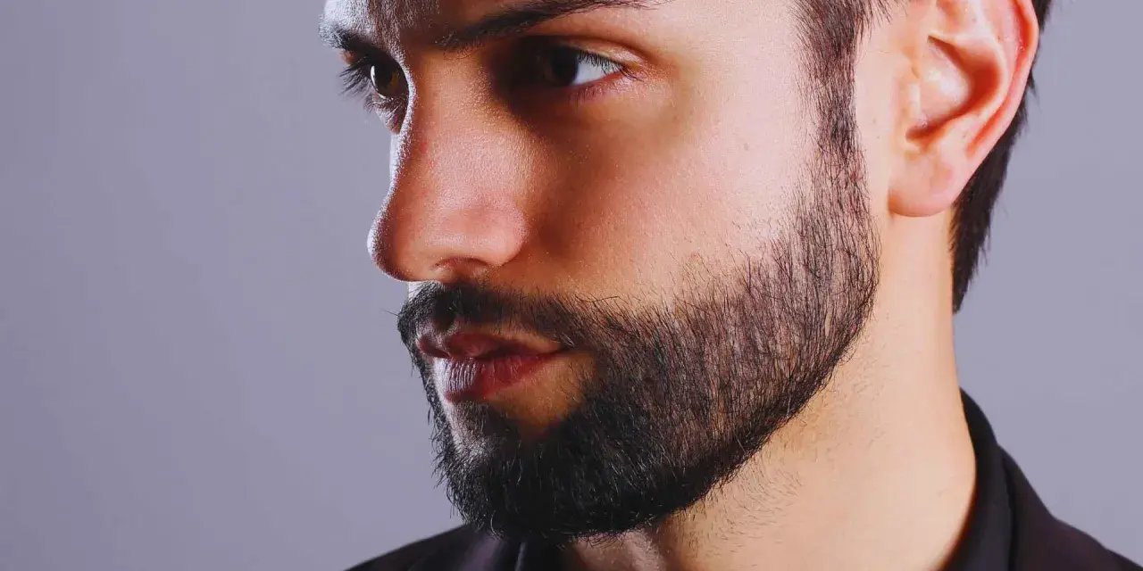 Primer plano de un hombre con barba cuidada, con un estilo fade beard que se difumina hacia las mejillas.