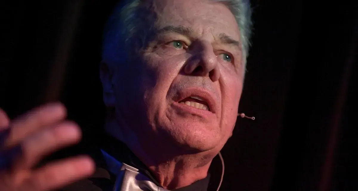Emilian Kamiński, znany z wielu filmów, w eleganckim stroju z muszką, przemawia na scenie.