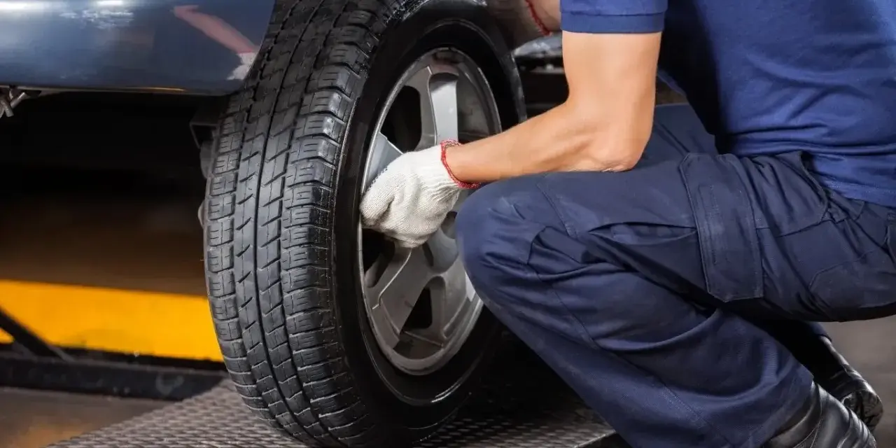 Mechanik w białych rękawiczkach dokręca śruby koła. Czas pomyśleć, kiedy wymienić opony na letnie.