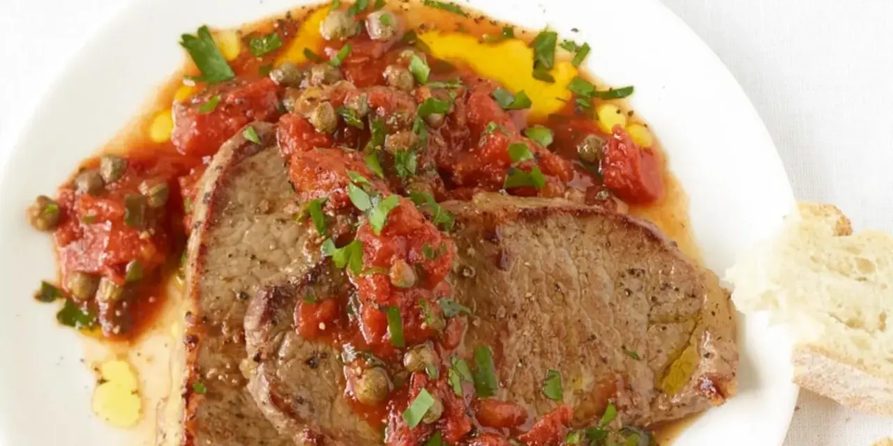 Zwei saftige Scheiben Rindfleisch, bedeckt mit einer würzigen Tomaten-Kapern-Sauce, serviert mit Brot. Ein authentisches Gericht im Stil Pizzaiola original italienisch.