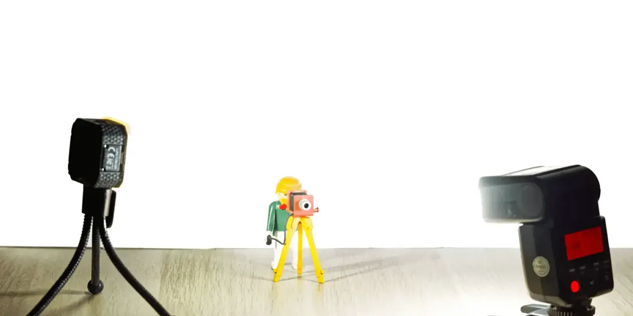 Une figurine Playmobil prend une photo avec un appareil sur trépied. Une autre caméra et un flash sont présents. Vue macro.
