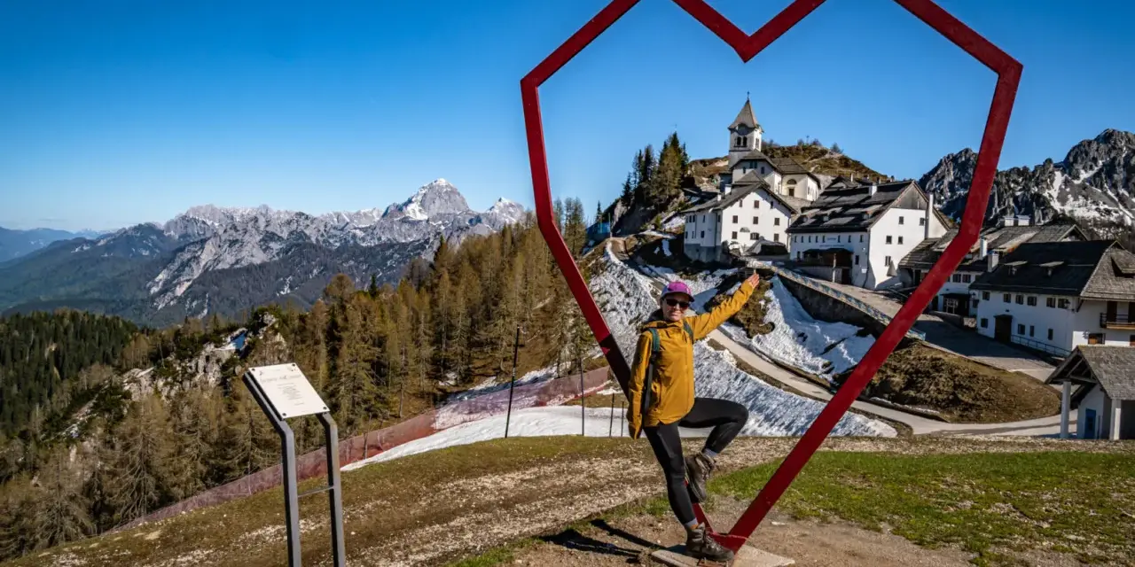 Kobieta w sercu z widokiem na górską wioskę Monte Lussari.