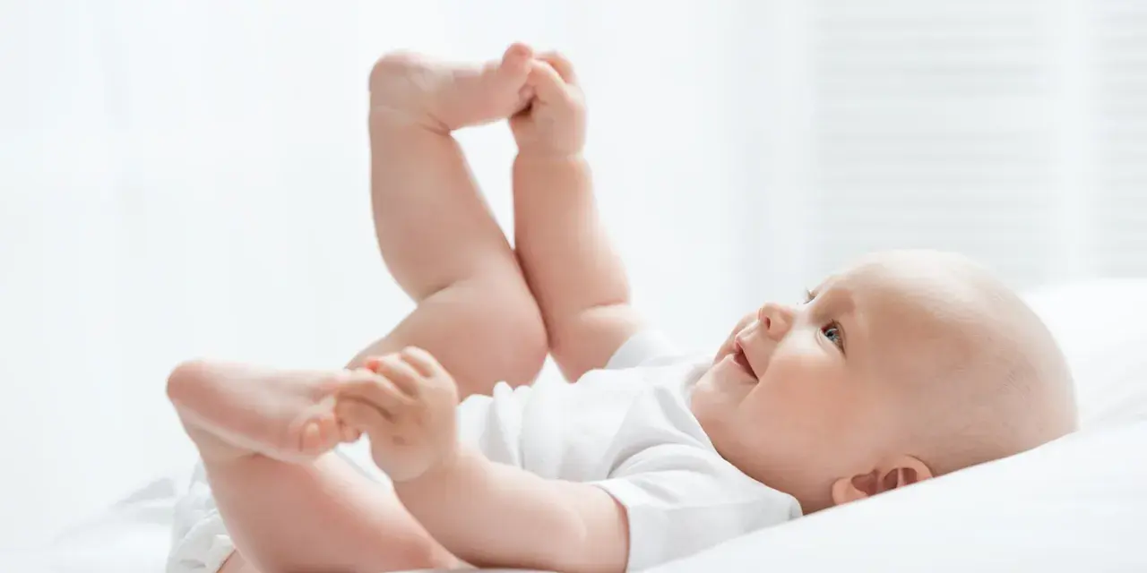 Uśmiechnięte dziecko leży na plecach, podnosząc nóżki. Czas na zmianę pampersów na większe, gdy maluch rośnie.
