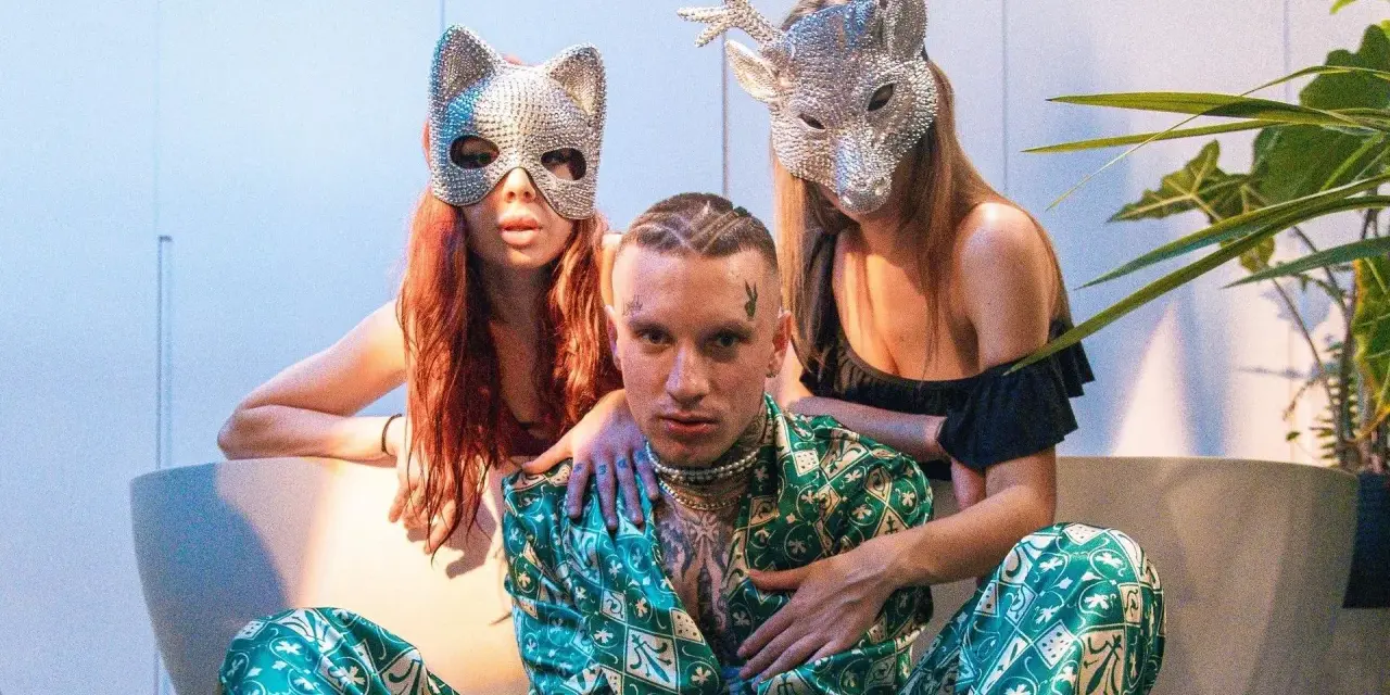 Smolasty z dużymi oczami w otoczeniu dwóch kobiet w błyszczących maskach.