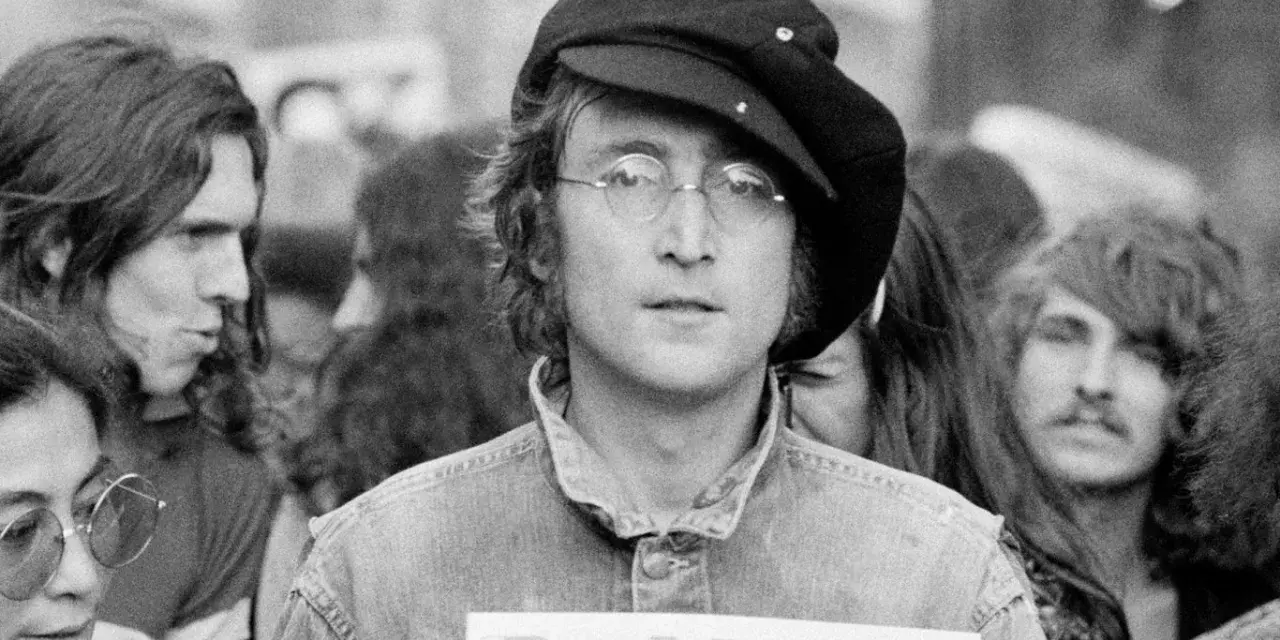 John Lennon w czapce i okularach, trzymający plakat "Red Mole". W tle inni ludzie, być może fani jego utworów.