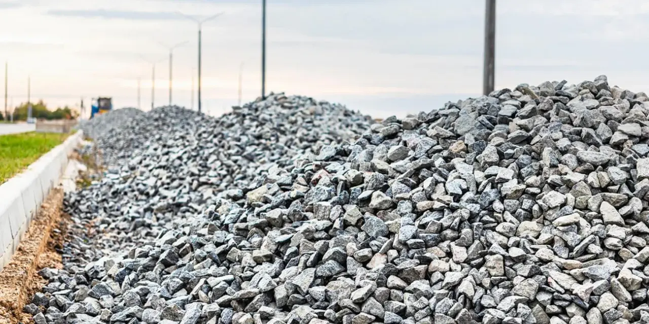Stos kruszywa, idealnego jako składnik betonu B25, na tle słupów oświetleniowych i nieba.