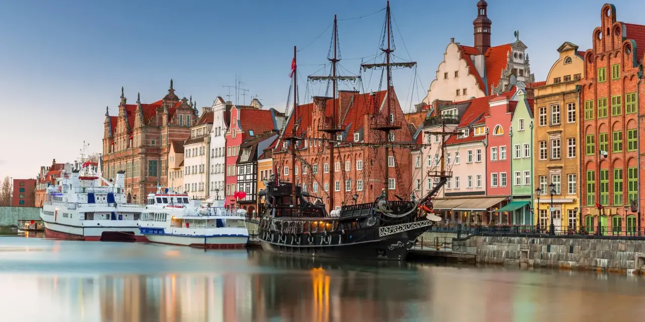 Gdański port z żaglowcem i kolorowymi kamienicami. To miejsce, co warto zwiedzić w Polsce, zachwyca historią i widokami.