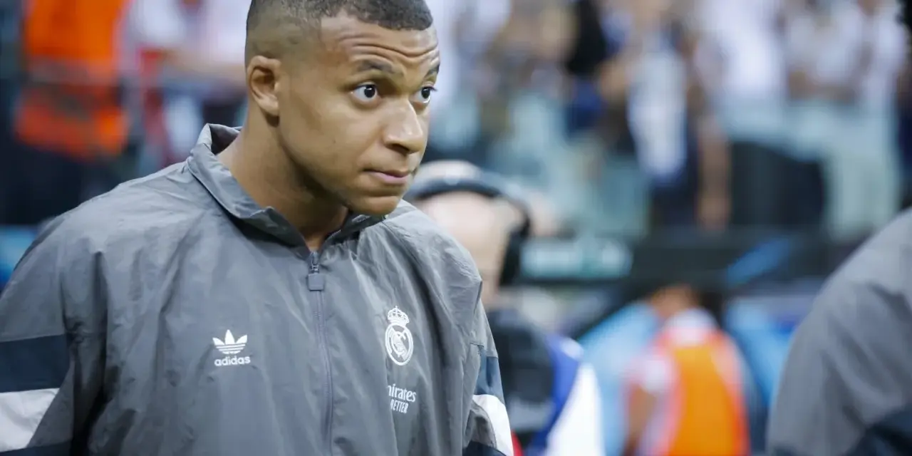 Kylian Mbappé w szarej kurtce z logo Realu Madryt, gotowy do gry.