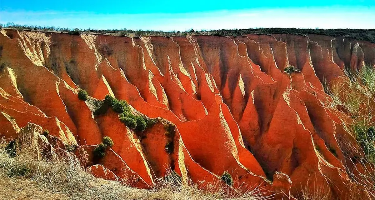 Impresionantes cárcavas en España, con formaciones rojizas y vegetación escasa bajo un cielo azul intenso.