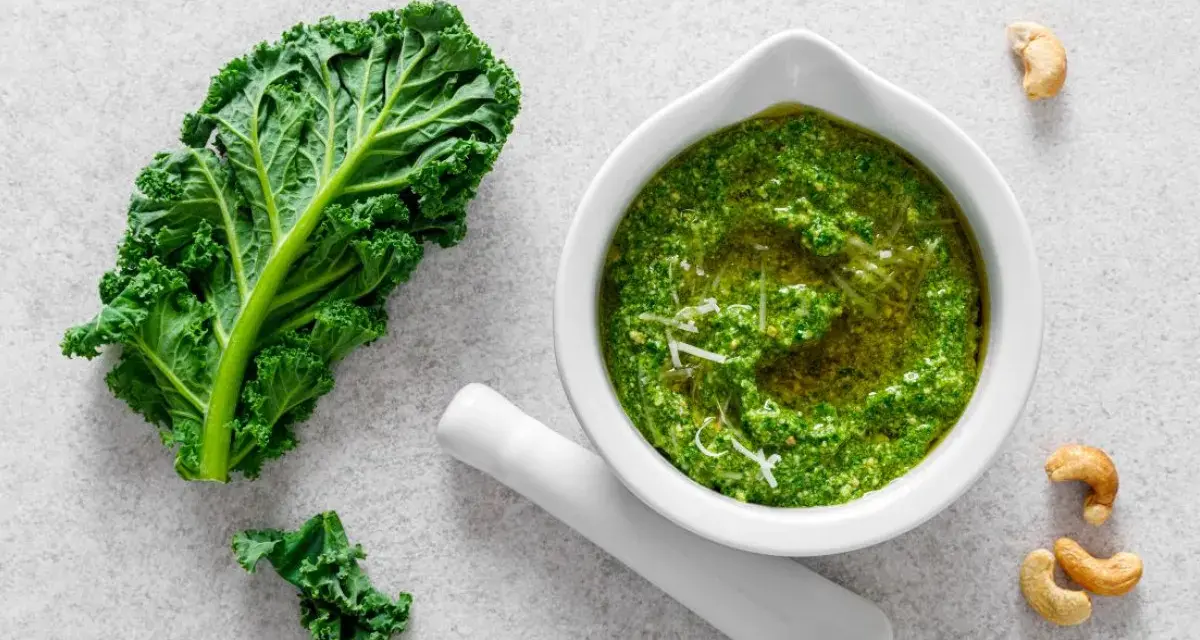 Pesto z jarmużu do słoika, gotowe do przechowywania. Obok liść jarmużu i orzechy nerkowca.